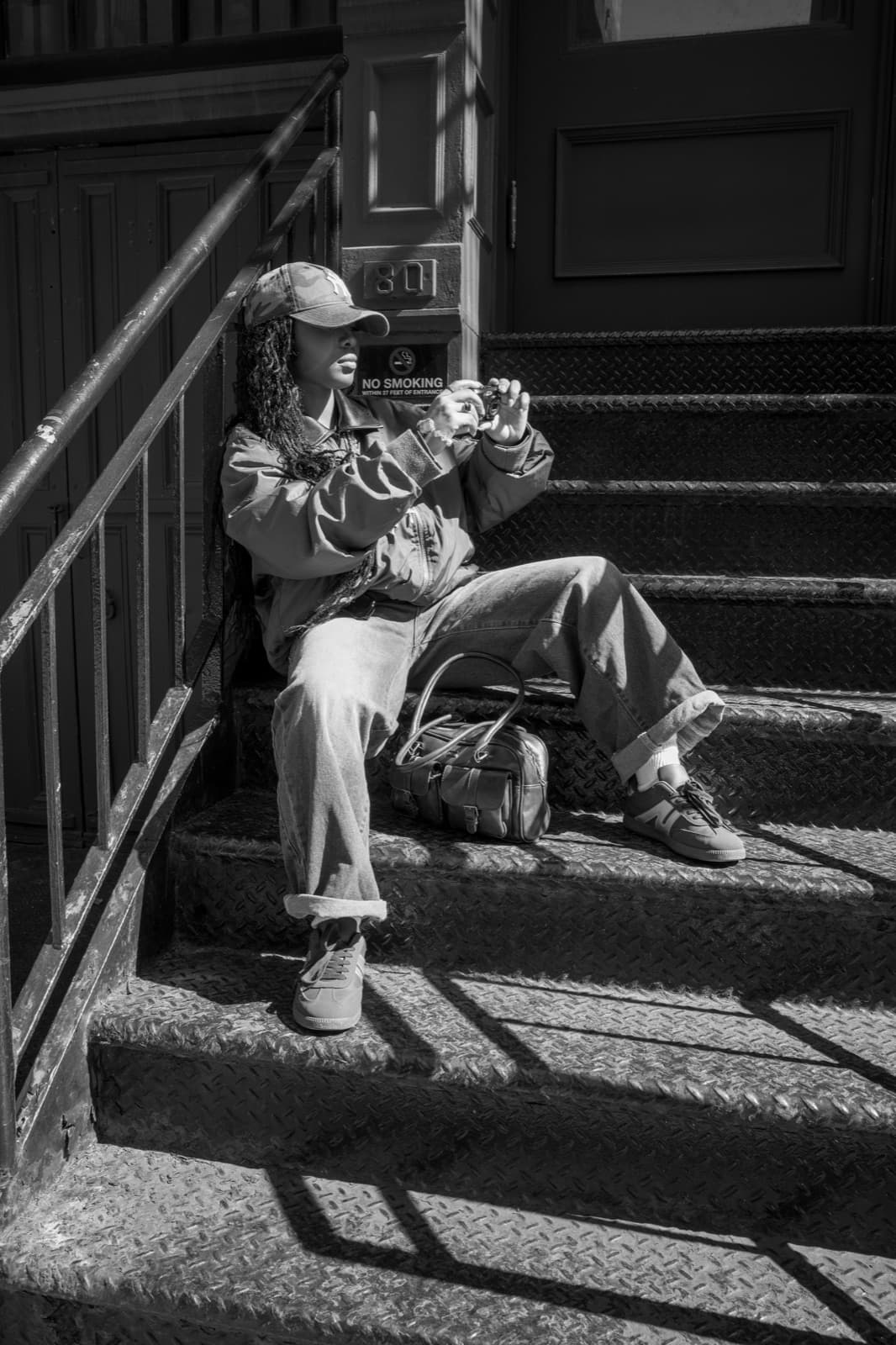 A person in a cap sits in sharp sunlight on a New York stoop.