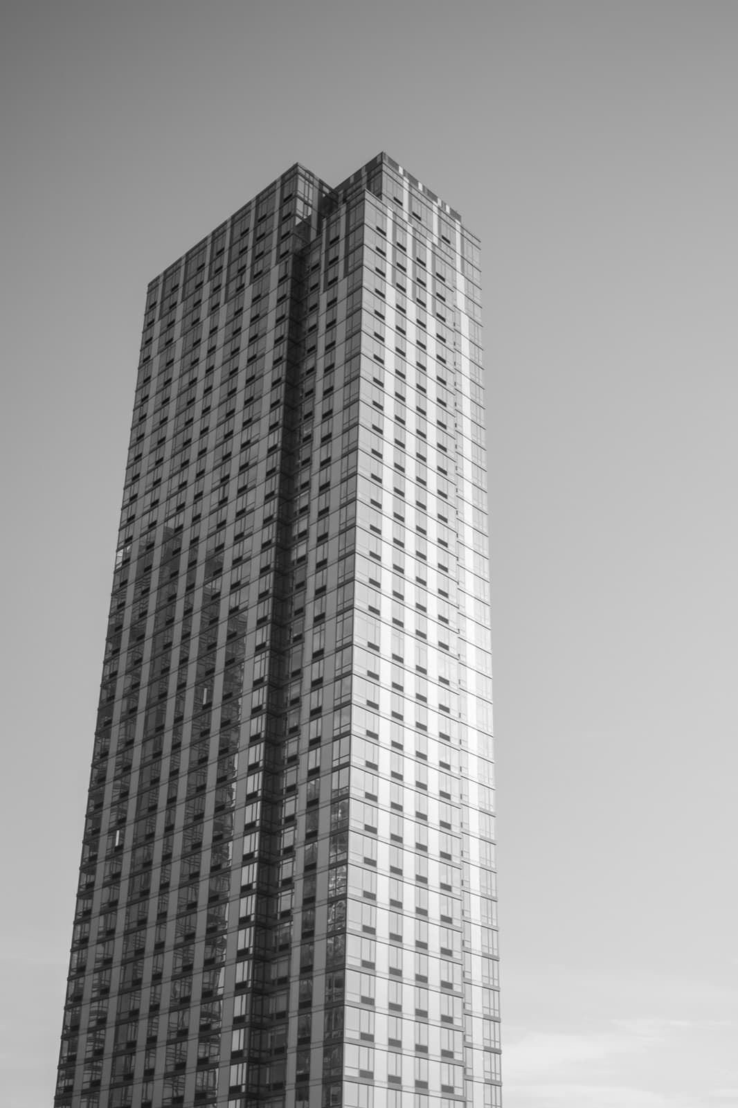 A slender high-rise tower rises alone into a pale sky in black and white.