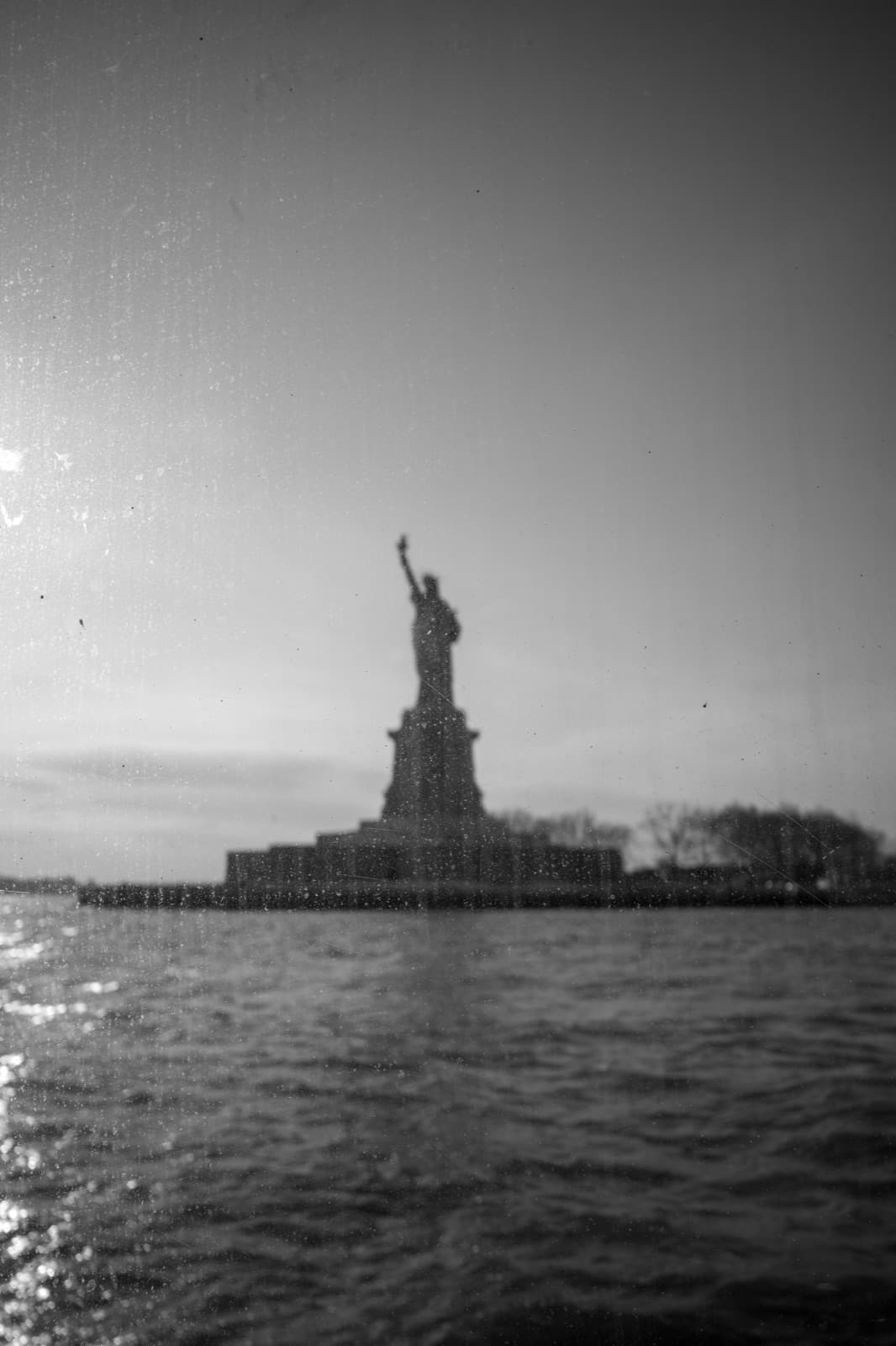 The Statue of Liberty appears softly across choppy harbor water in black and white.