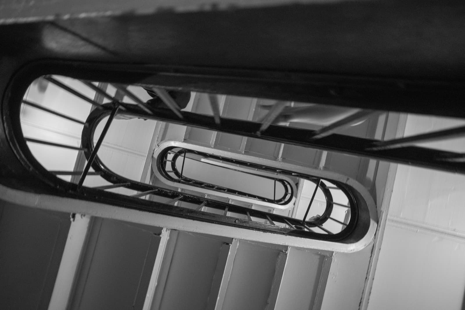A spiral stairwell coils through an oval opening in a graphic black-and-white view.