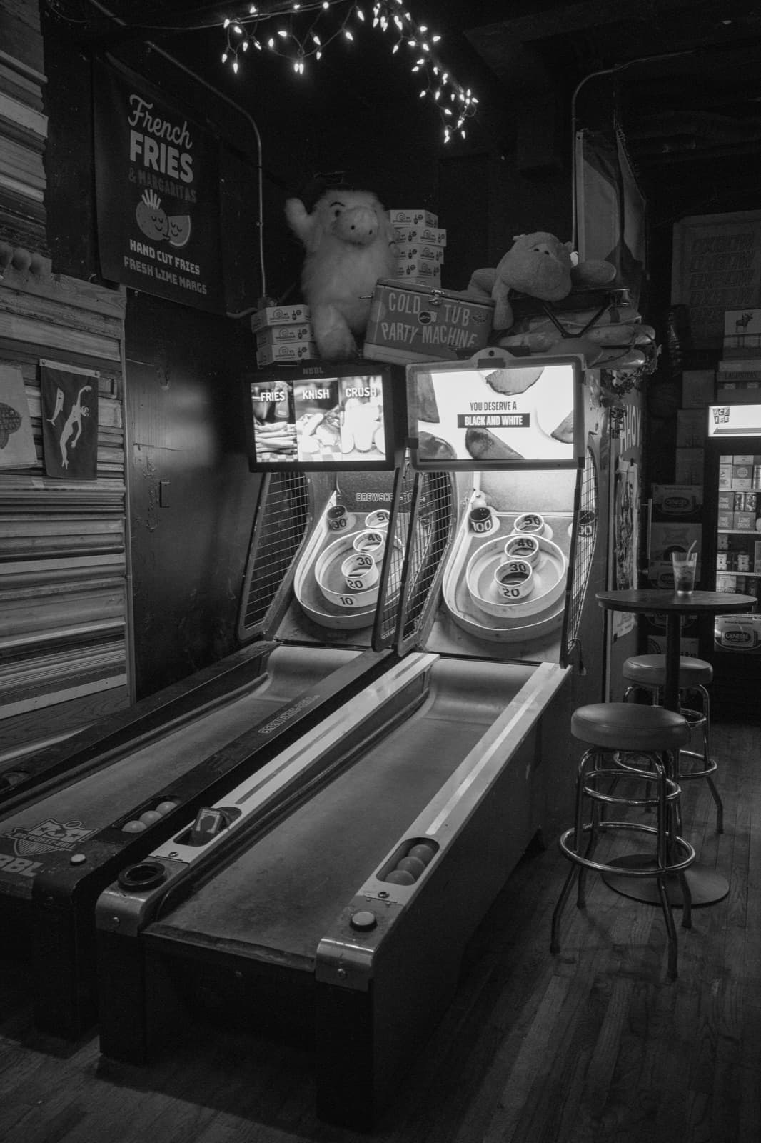 A row of illuminated skee-ball lanes recedes into a dim arcade.