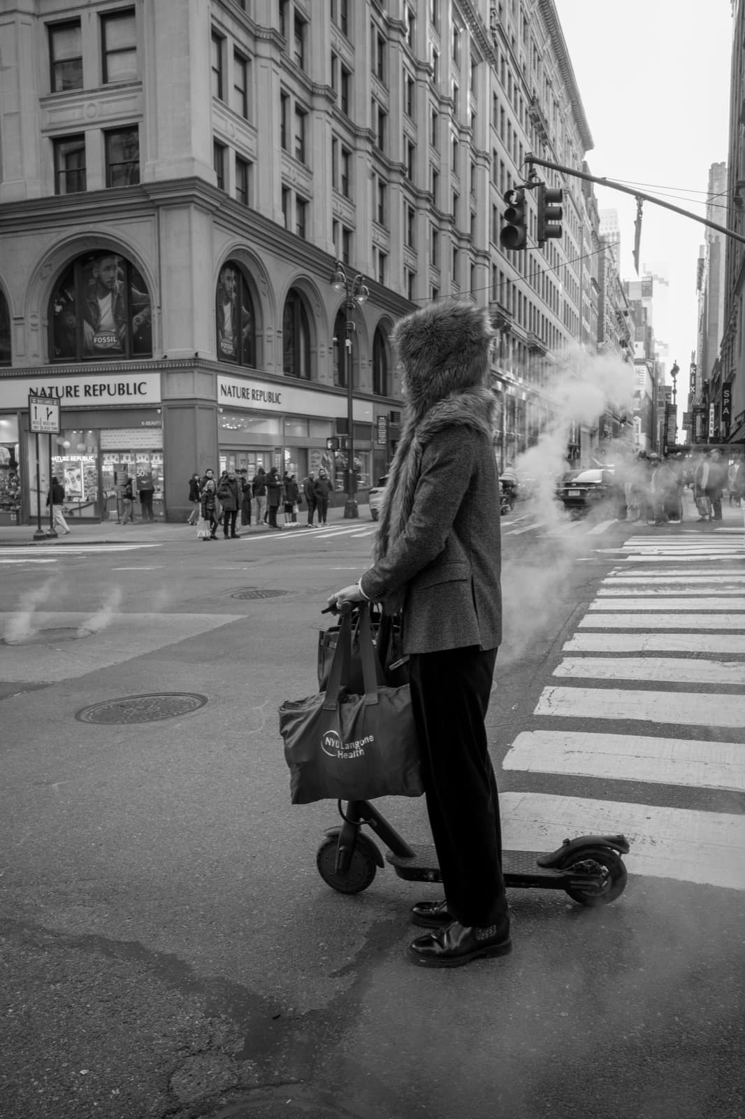 A woman pauses with a mobility scooter beside a steaming New York crosswalk.