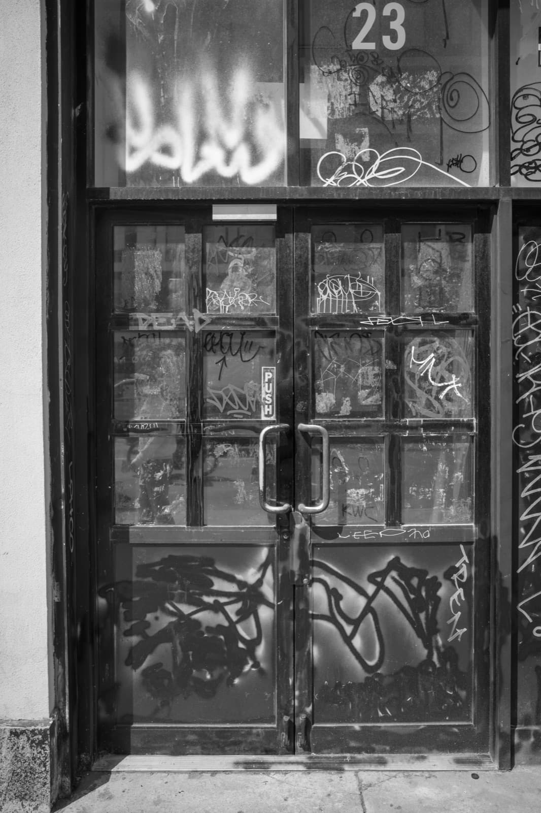A worn doorway marked 23 is layered with graffiti, stickers, and reflections.