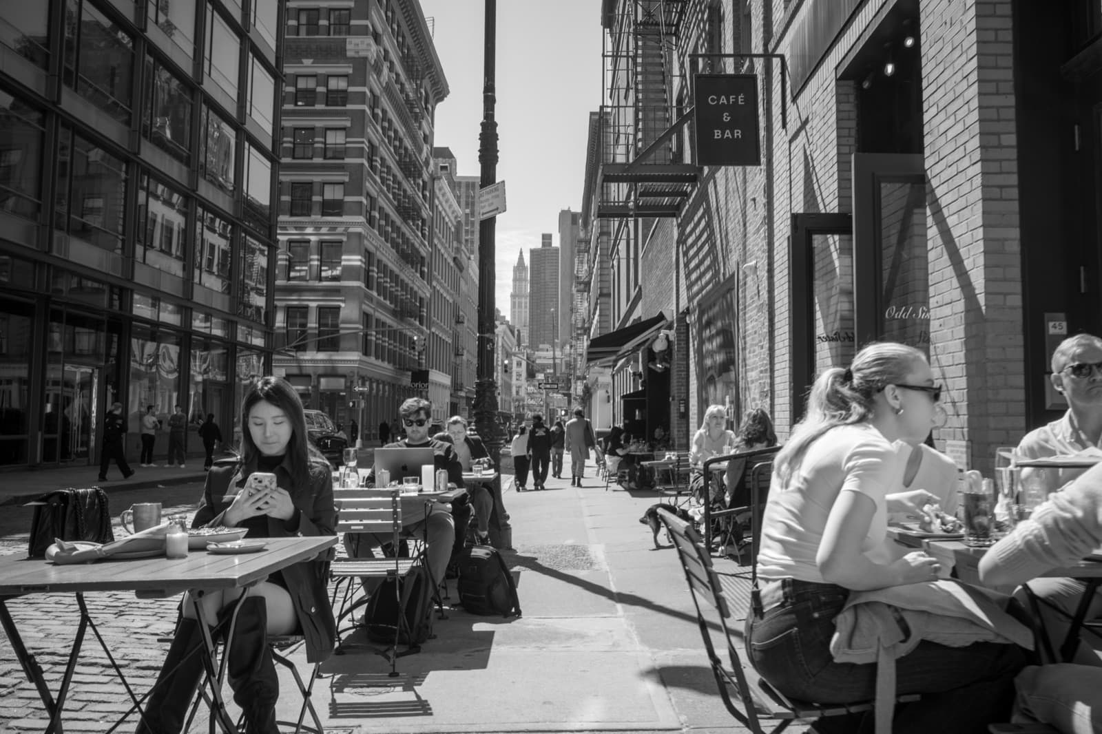 Diners gather at sidewalk tables along a sunlit New York avenue.