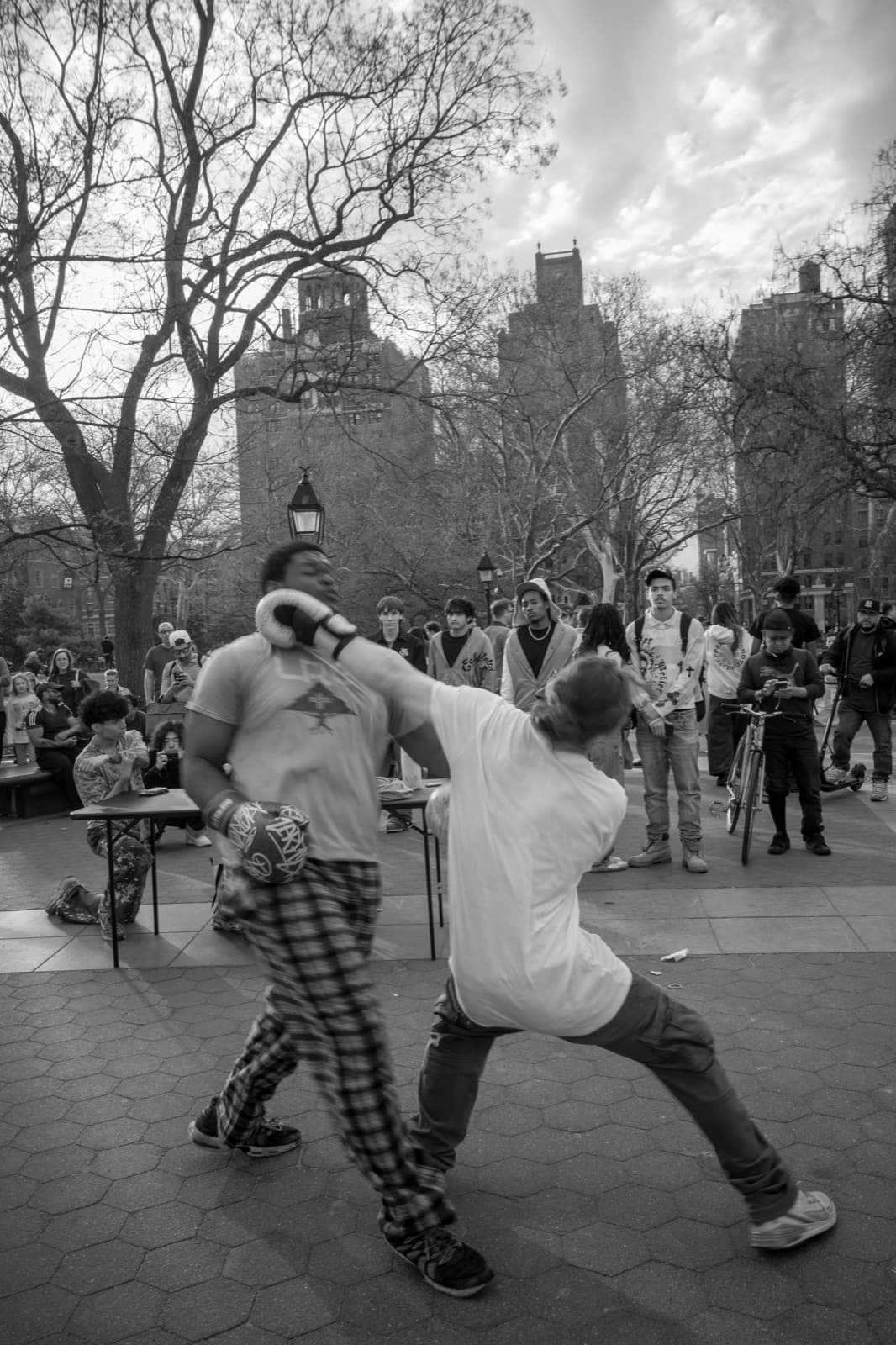Two costumed performers face each other while a park crowd watches in black and white.