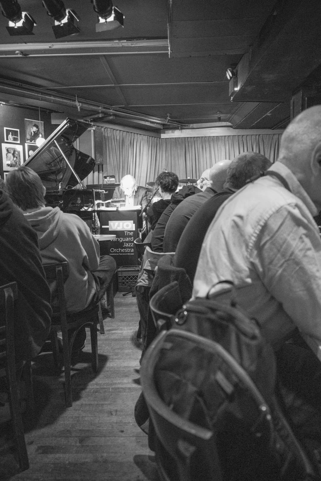 A packed bar counter fills the frame beneath low lights and a broad hat.
