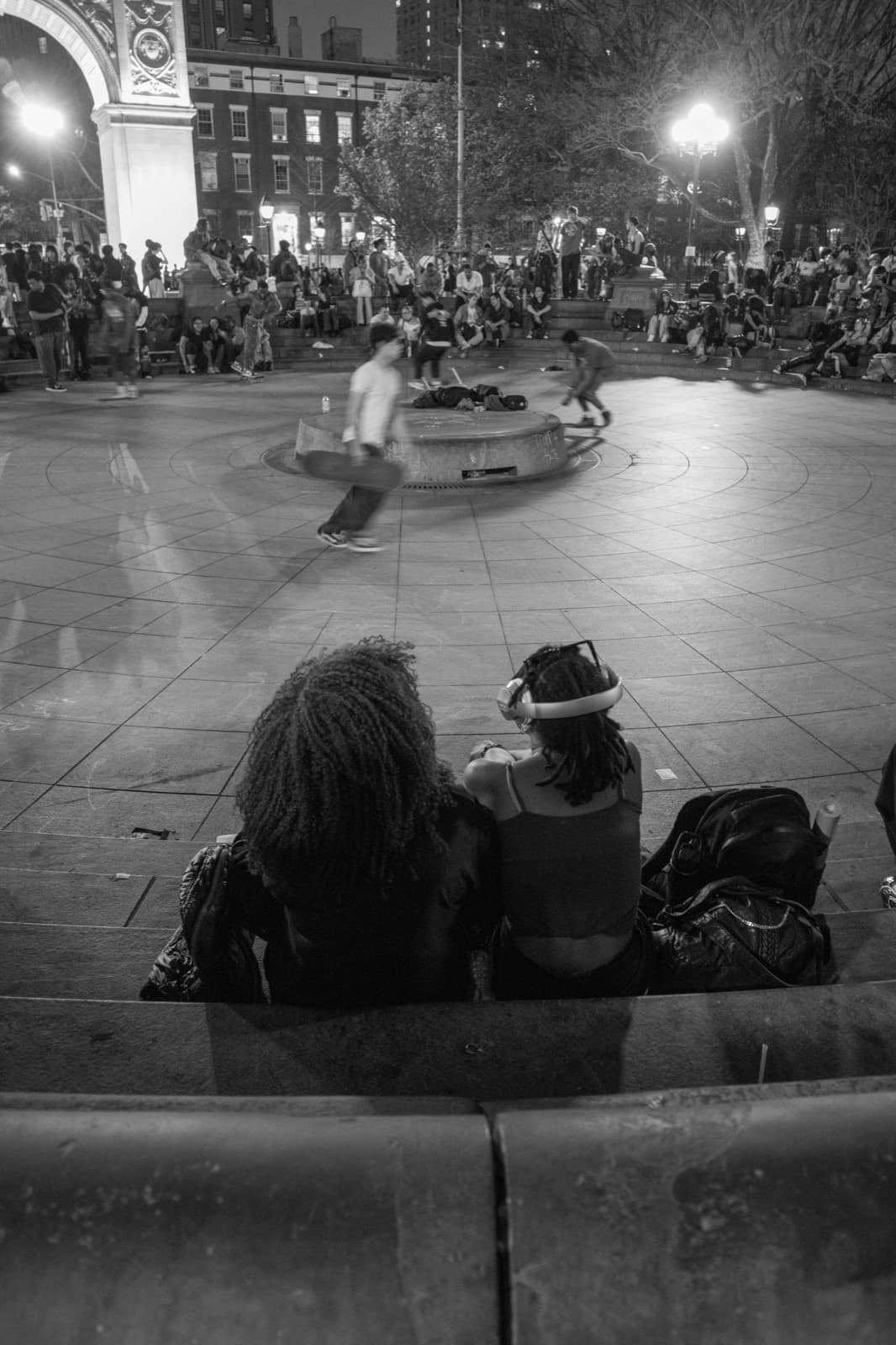 A performer spins on a low platform while a nighttime plaza crowd watches.