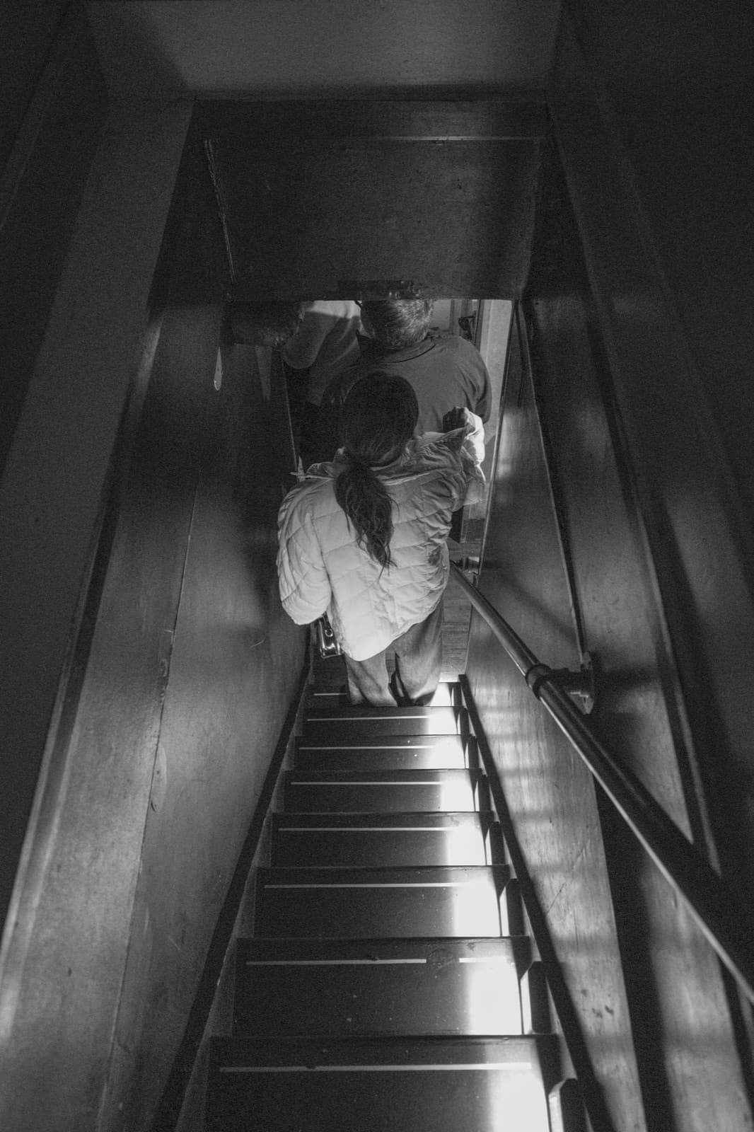A person descends a narrow stairwell through a shaft of overhead light.