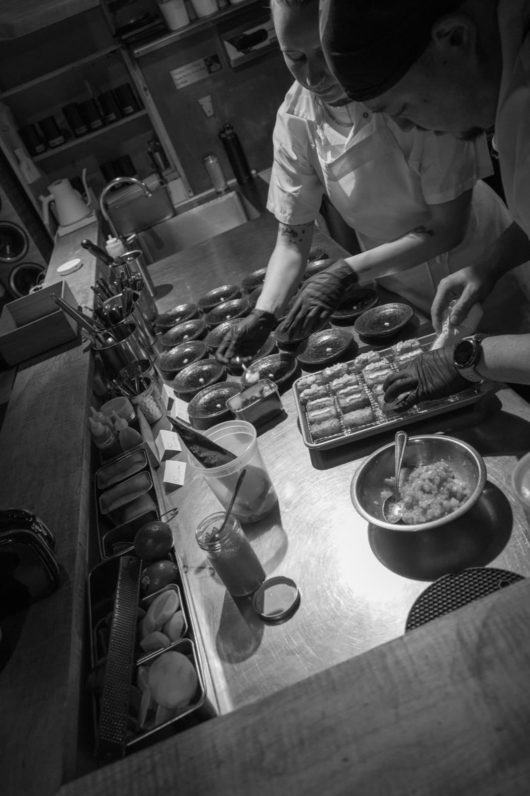 A chef arranges dishes behind a busy sushi counter in black and white.
