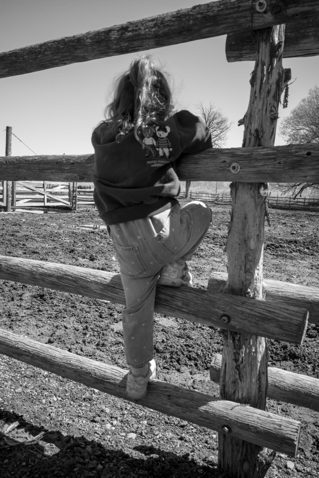 A woman climbs a split-rail fence beneath a simple wooden gate.