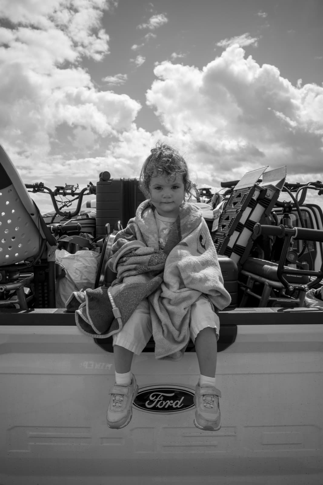 A child wrapped in a blanket sits on the tailgate of a vintage Ford truck.