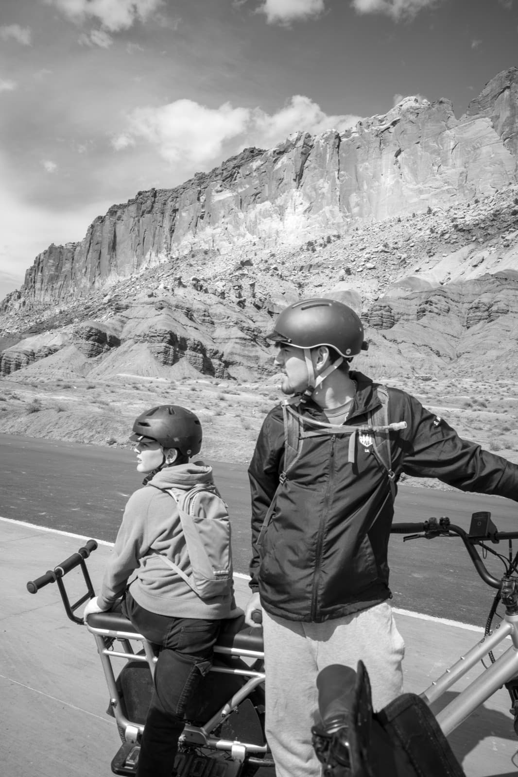 An adult and child in helmets stand with bicycles before a pale canyon wall.