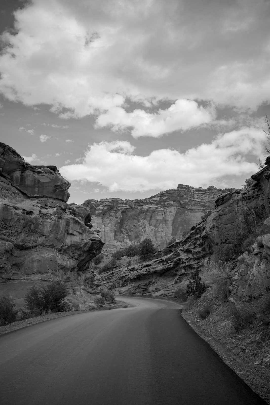 An empty highway bends between weathered canyon walls beneath bright clouds.