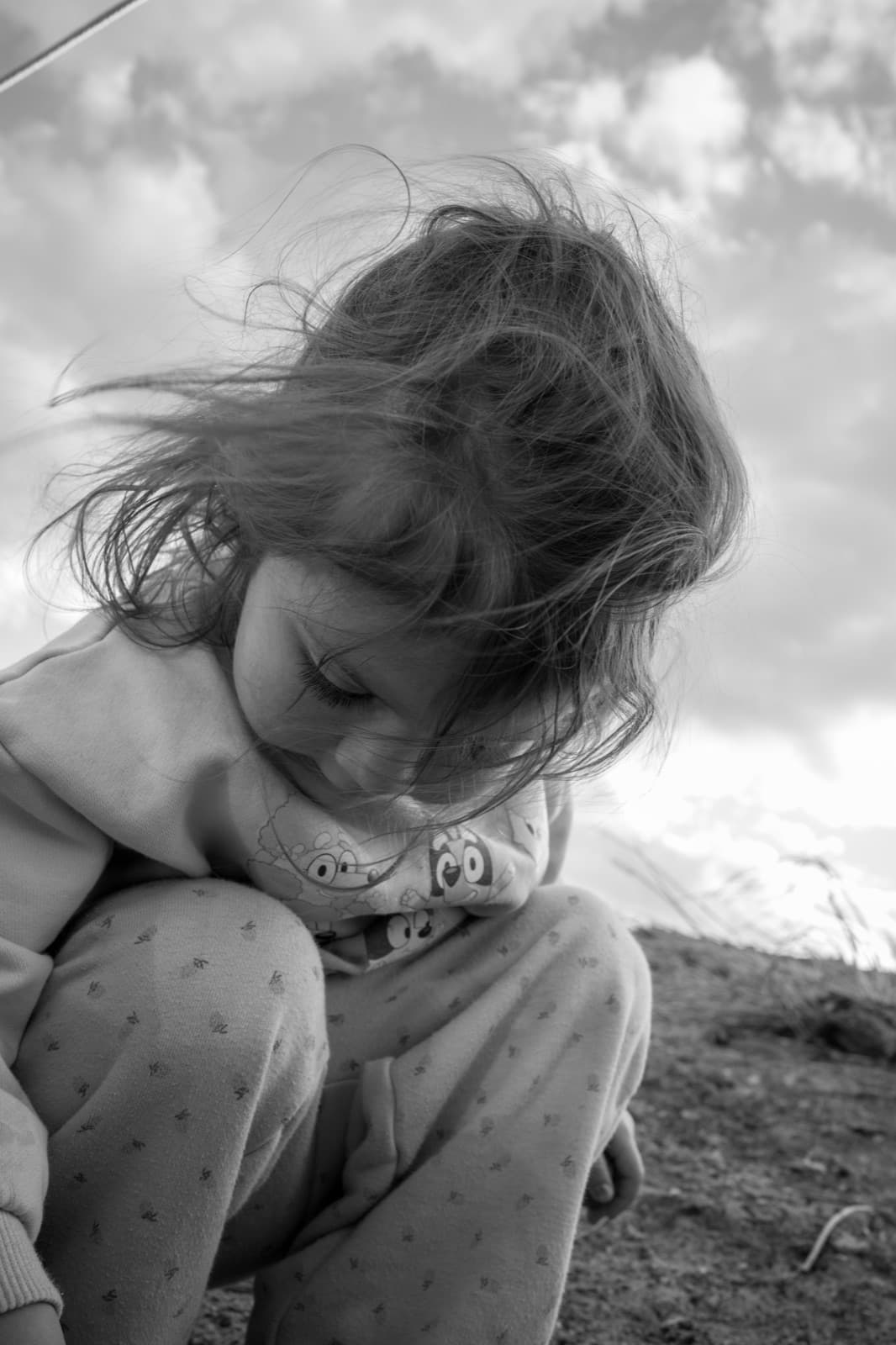 A child looks down as wind lifts their hair against an open sky.