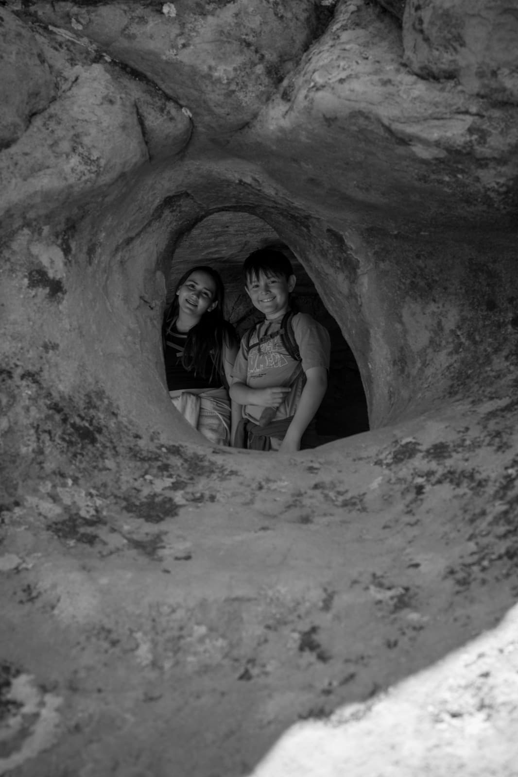 Three people peer through a rounded opening carved into a rock wall.