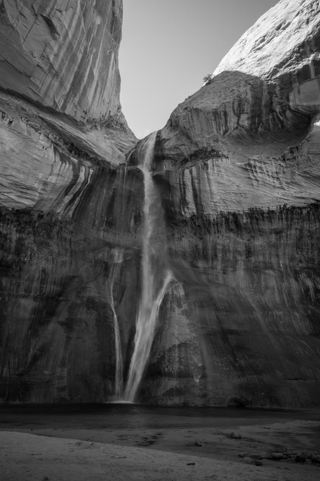 A tall waterfall descends a streaked rock face into a shadowed canyon.