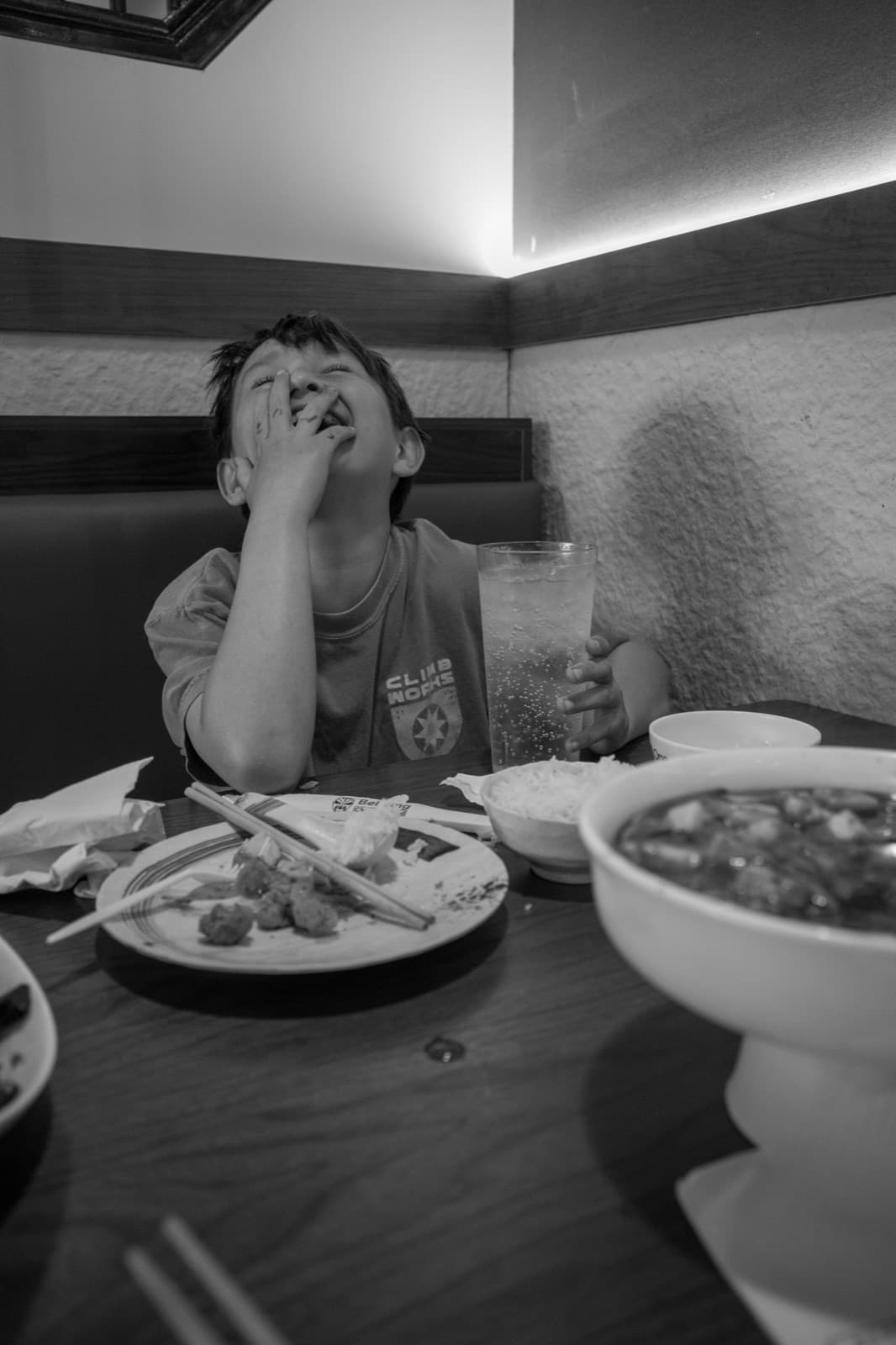 A child rests a hand near their face at a restaurant table in black and white.