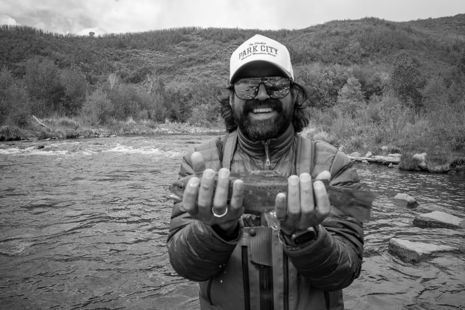 Carlos sits beside a river and holds two rounded stones toward the camera.
