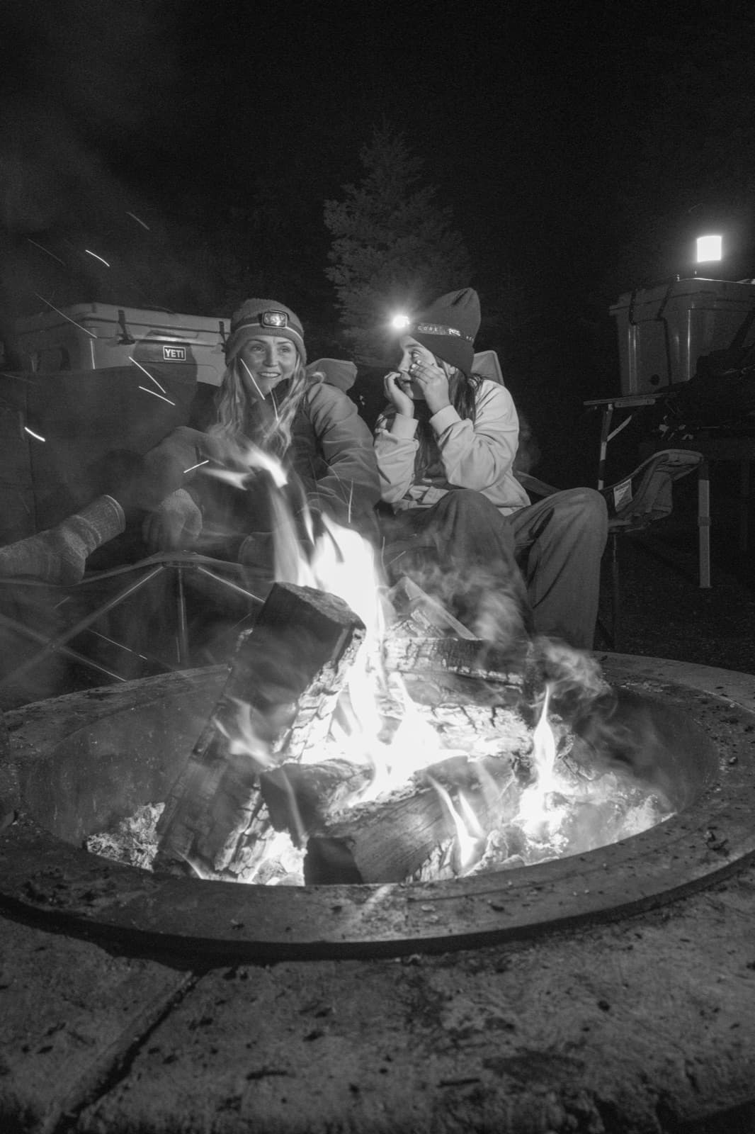 Family and friends gather around a bright campfire after dark.