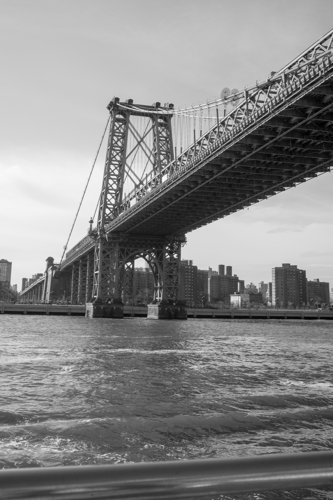 A suspension bridge spans the river beneath a broad sky in a black-and-white city view.
