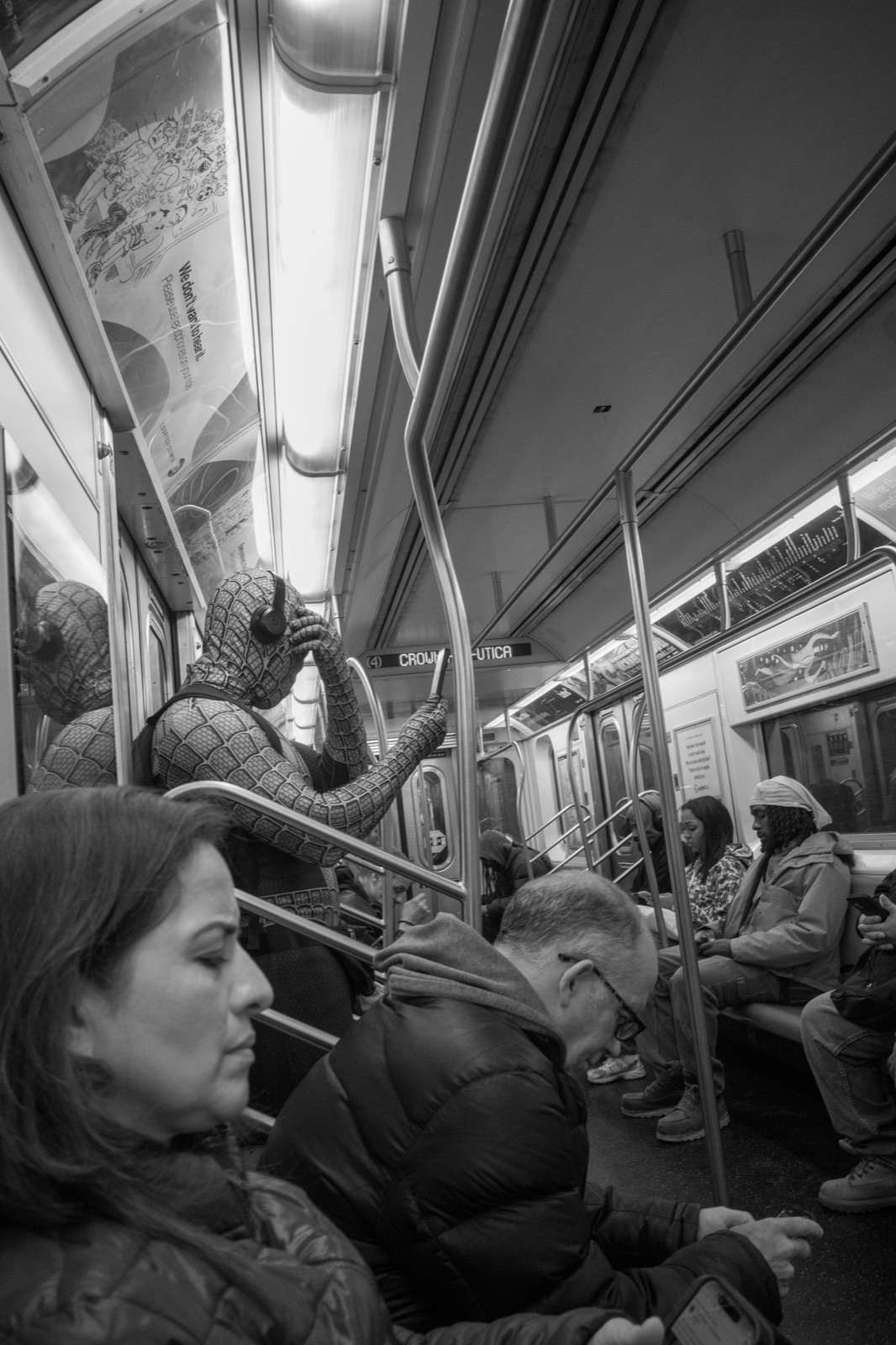 Passengers fill a New York subway car, seen from within the aisle in black and white.